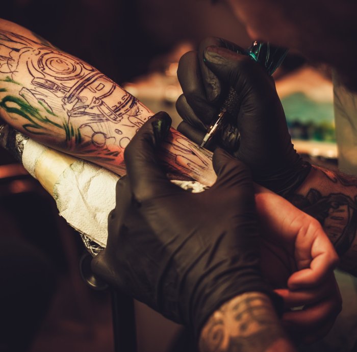 Tattoo artist makes a tattoo on a man's hand.
