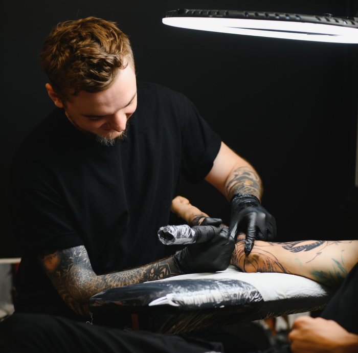 tattooist with his machine tattooing on the arm with the design drawn, concept of art and design